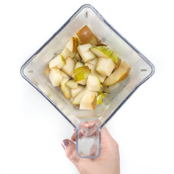 Hand holding a blender with steamed pears.