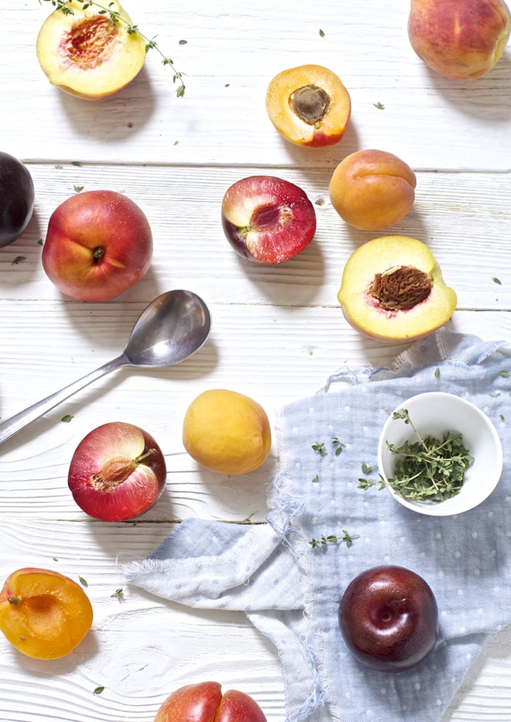 stone fruit and thyme scattered on top of white wooden board.