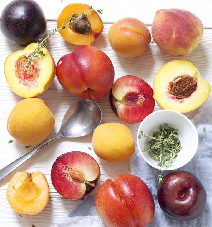 Scatter of stone fruit and thyme on a white wooden board.