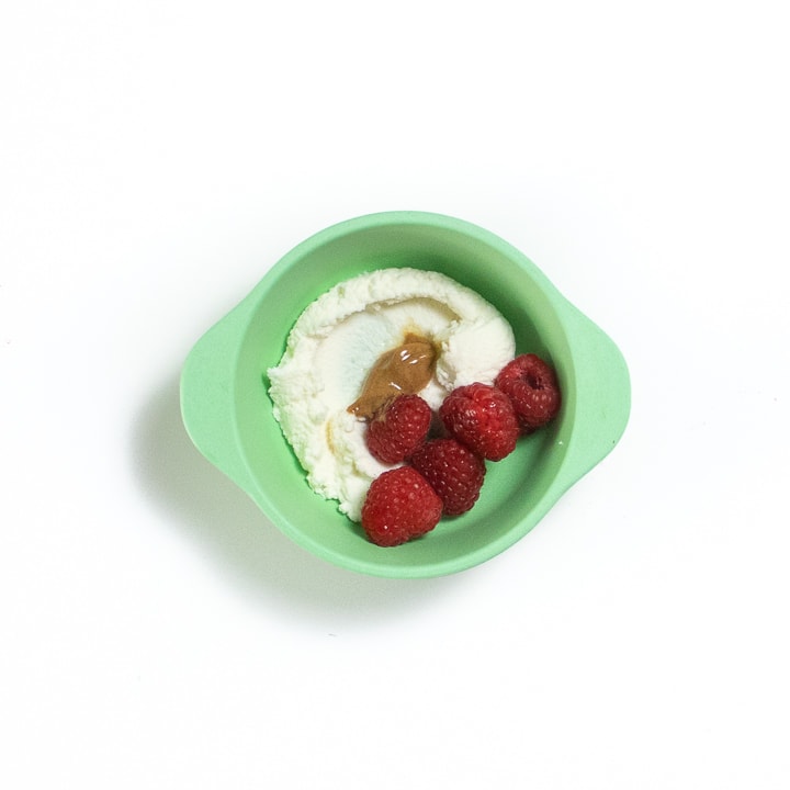 Green bowl full of a few raspberries, ricotta and nut butter.