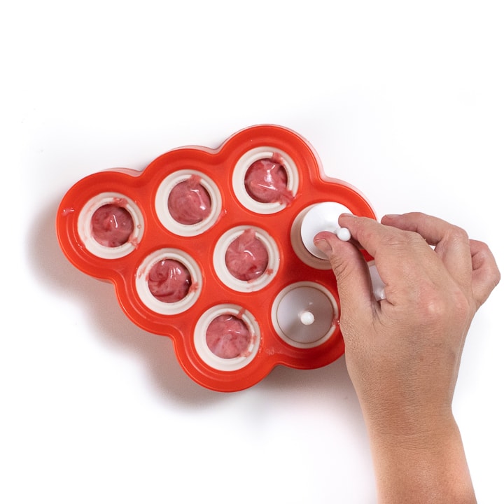 Handing putting a white popsicle stick inside a red tray of popsicles.