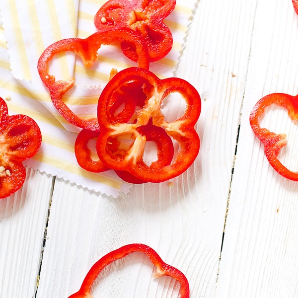 slices of red pepper laying on a white wooden board with a white and yellow napkin. 