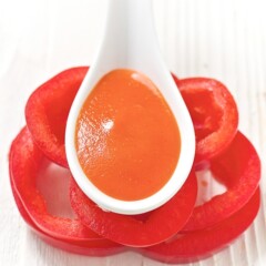 white spoon resting on top of a stack of red pepper slices. spoon has red pepper baby food recipe in it.