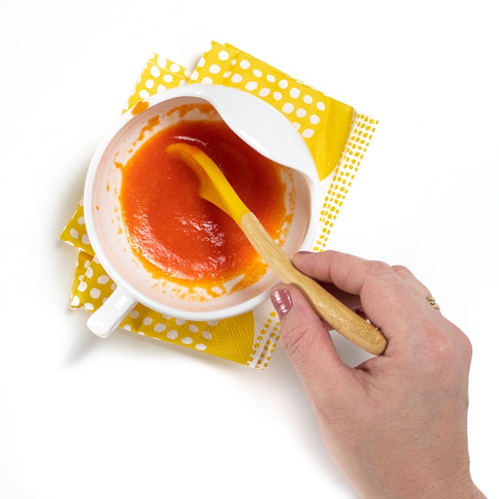 Hand stirring red pepper puree in a white bowl.