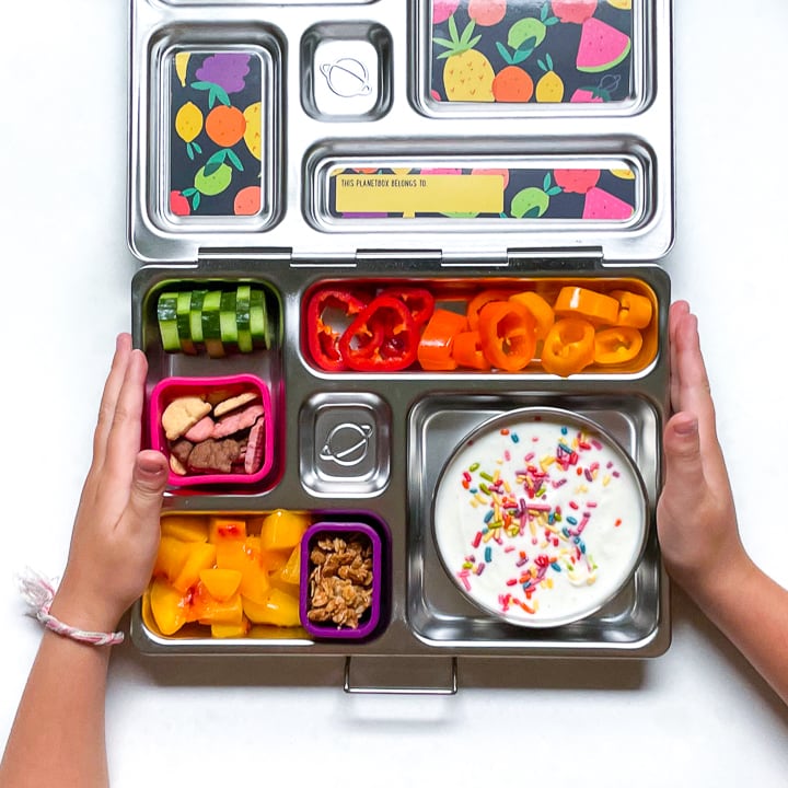 Small kids hands holding a metal lunch box filled with a healthy lunch.