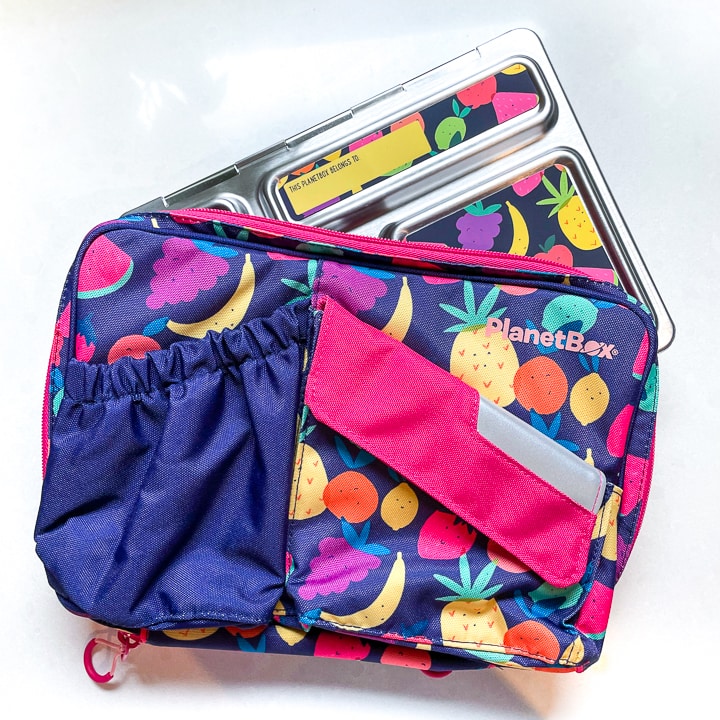 planetbox carrying case with fruit on a purple background with a silver lunch box sticking out of the top.