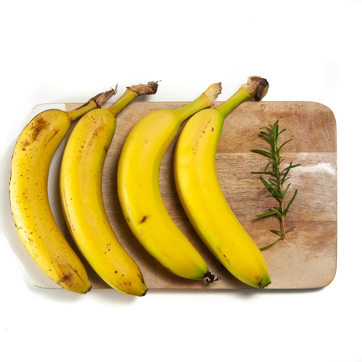 bananas lined up on a cutting board with rosemary ready to make into a homemade baby food meal. 