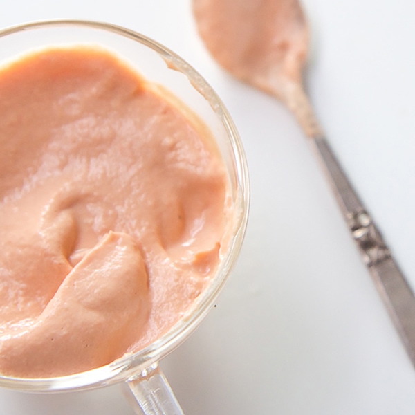 A small clear jar filled with a homemade salmon puree, with a silver spoon with puree on it nestled next to the jar.