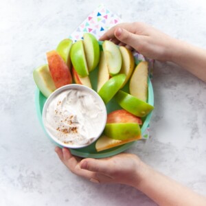 Hands holding a plate of apples and spiced dip.