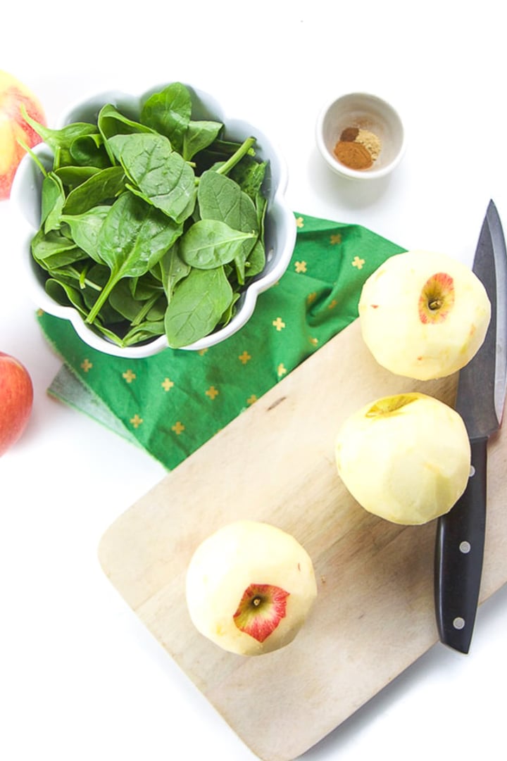 Cutting board with peeled apples on it with bowl of spinach next to it.