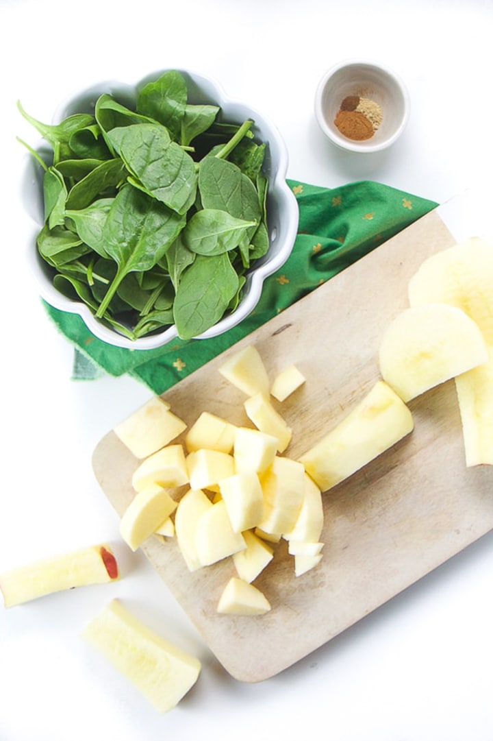 Cutting board with chopped apples and a white bowl of spinach sitting next to it.