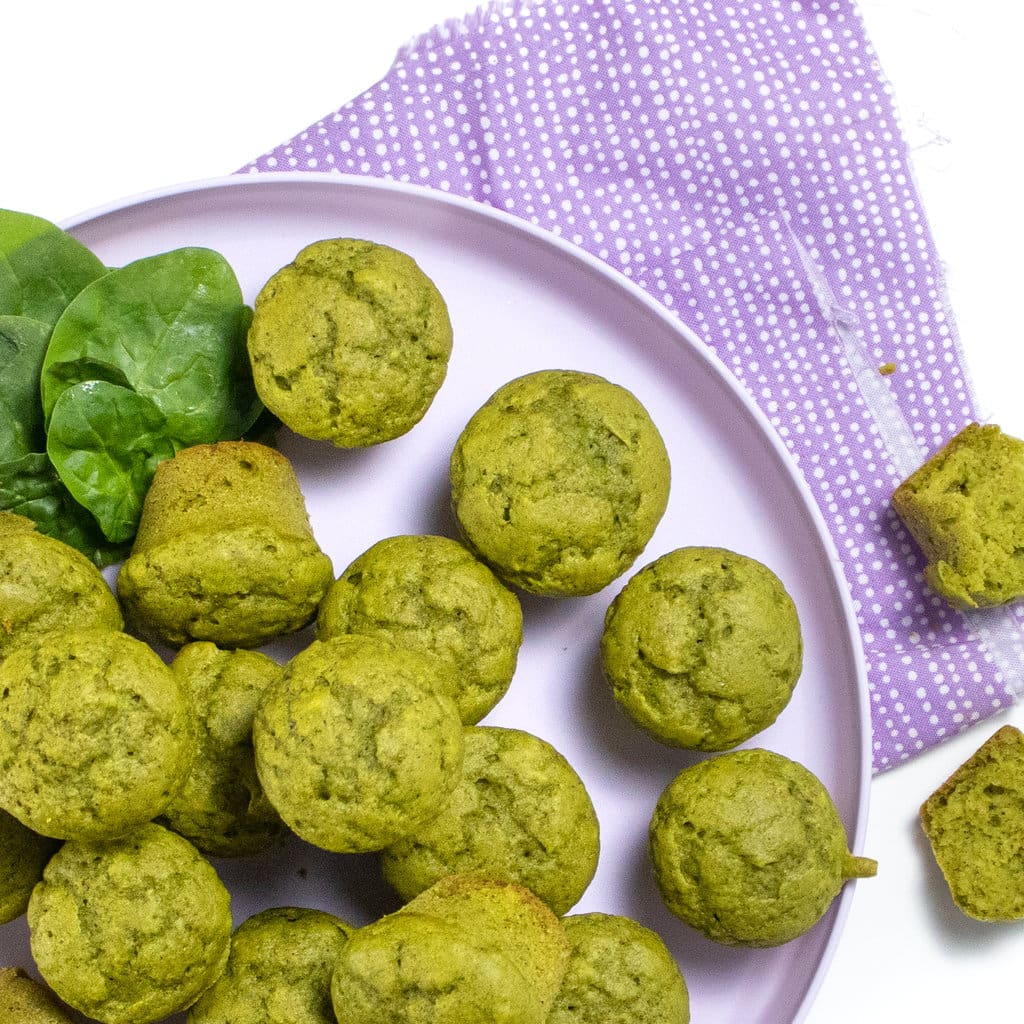 A purple kids play with spinach muffins with a purple napkin.