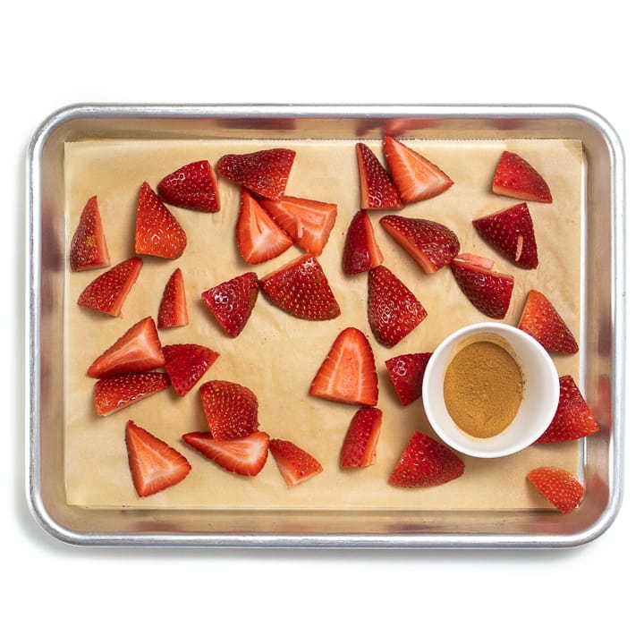 Baking sheet with fresh chopped strawberries and a small bowl of cinnamon.