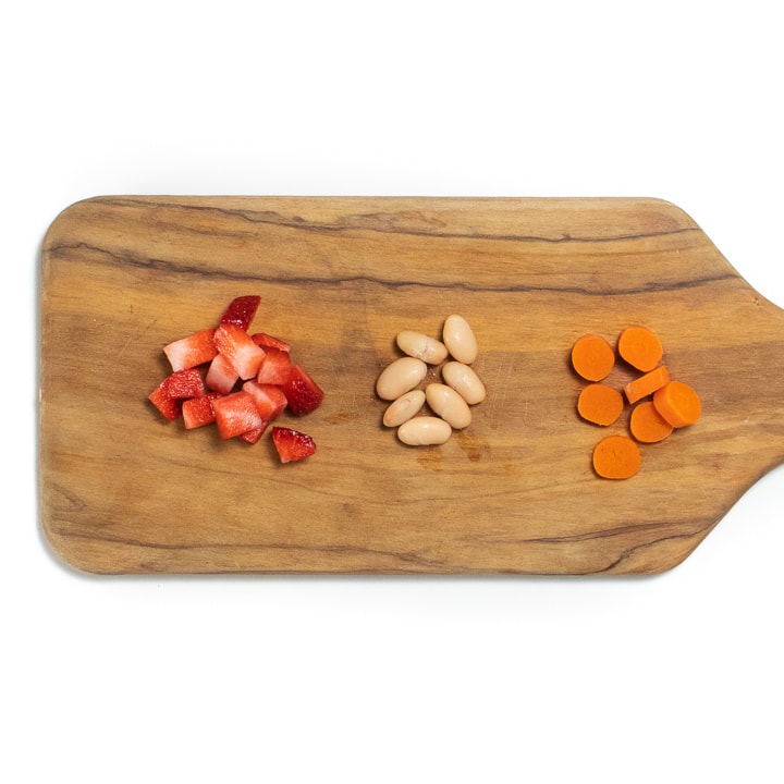 Cutting board with strawberries, beans and carrots.