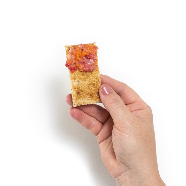 Hand holding a piece of toast with mashed strawberries, beans and carrots.