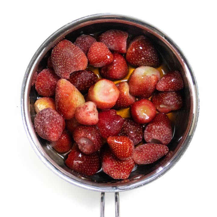 Silver saucepan with frozen strawberries, maple syrup and vanilla extract.