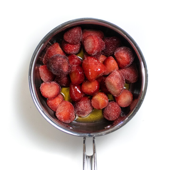 Silver sauce pan on the way background filled with frozen strawberries maple syrup and vanilla extract.