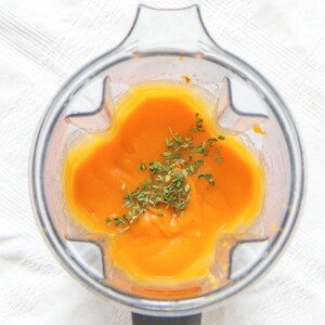 is a top view of a blender filled with sweet potato puree with a sprinkle of thyme on top - baby food for 4 months and up.