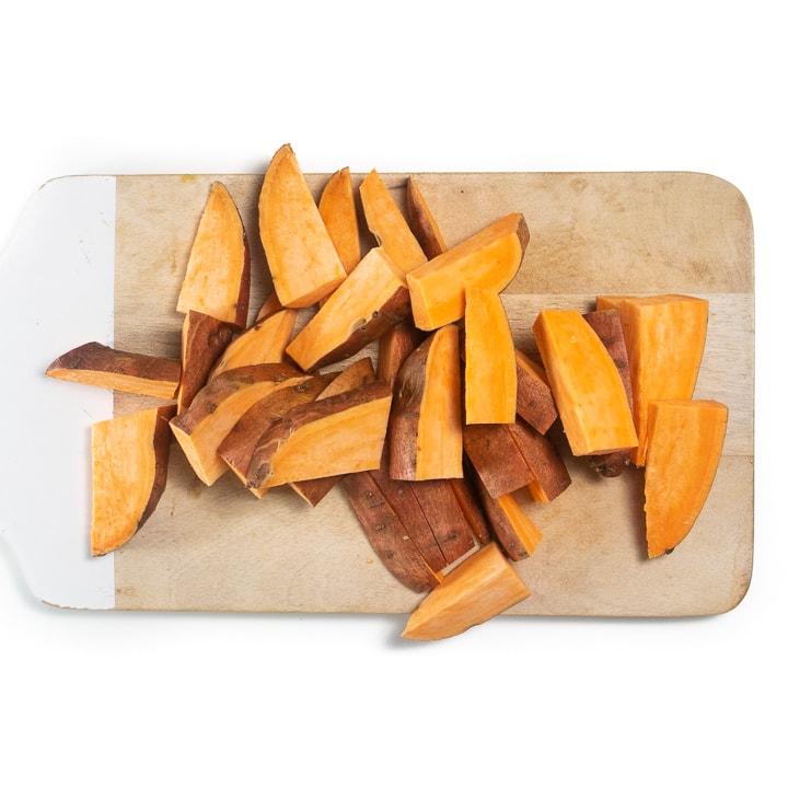 Cutting board with cut sweet potato wedges.