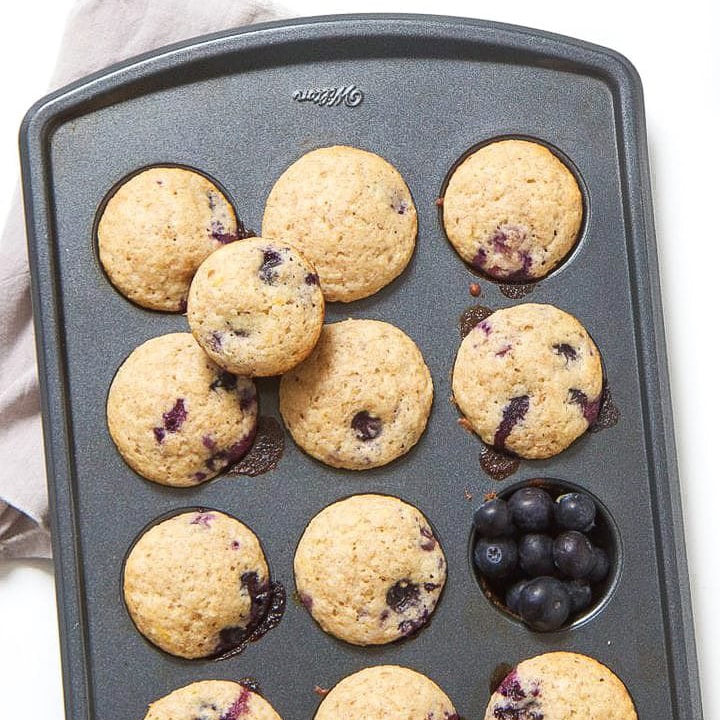 Mini muffins in a muffin tin with blueberries in a cup.