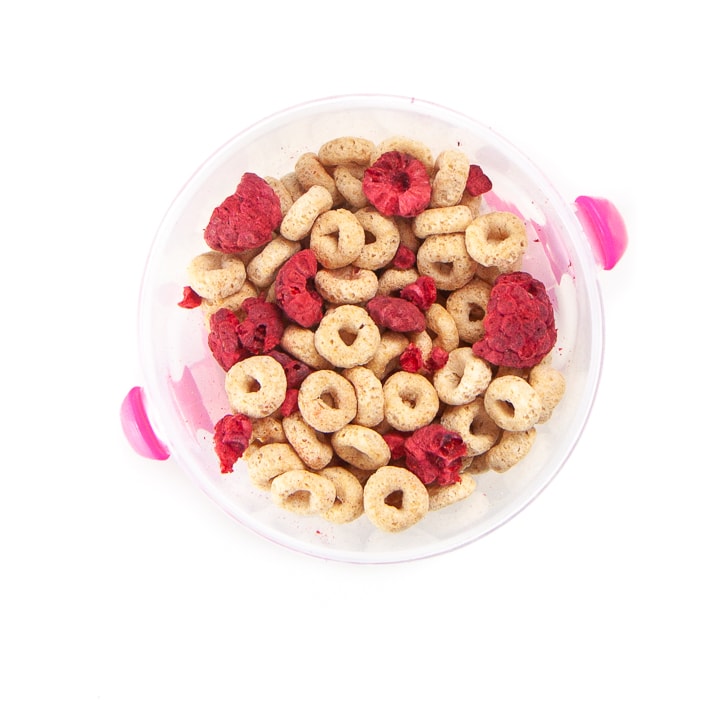 A toddler snack cup filled with cereal and freeze dried berries.