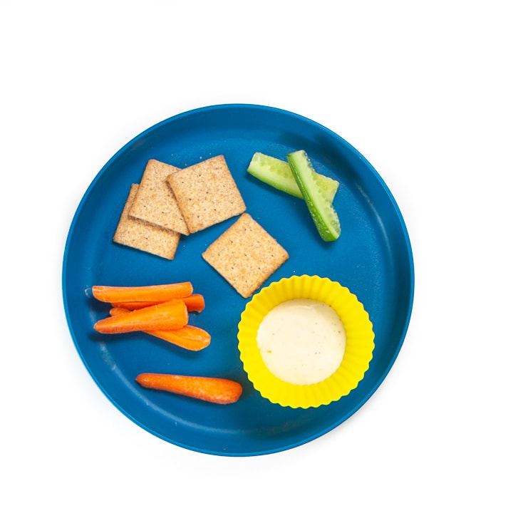 Toddler plate filled with cut veggies, crackers and dips. 