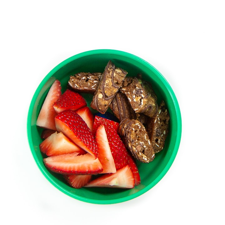 Green bowl filled with cut strawberries and chopped granola bars.