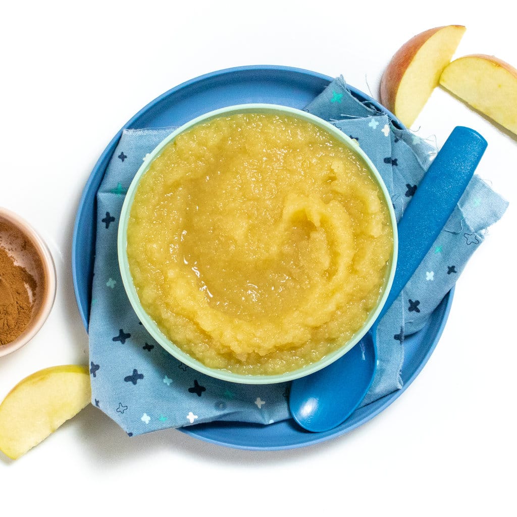 Blue kids plate and bowl with homemade applesauce and a scattering of apples, cinnamon and vanilla next to it.