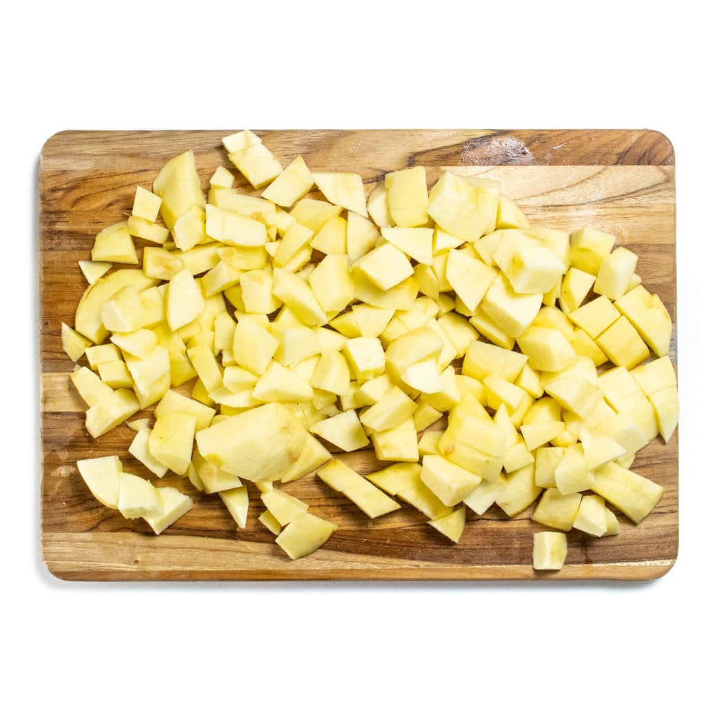 A wooden cutting board on a white countertop with chunks of apples on it.