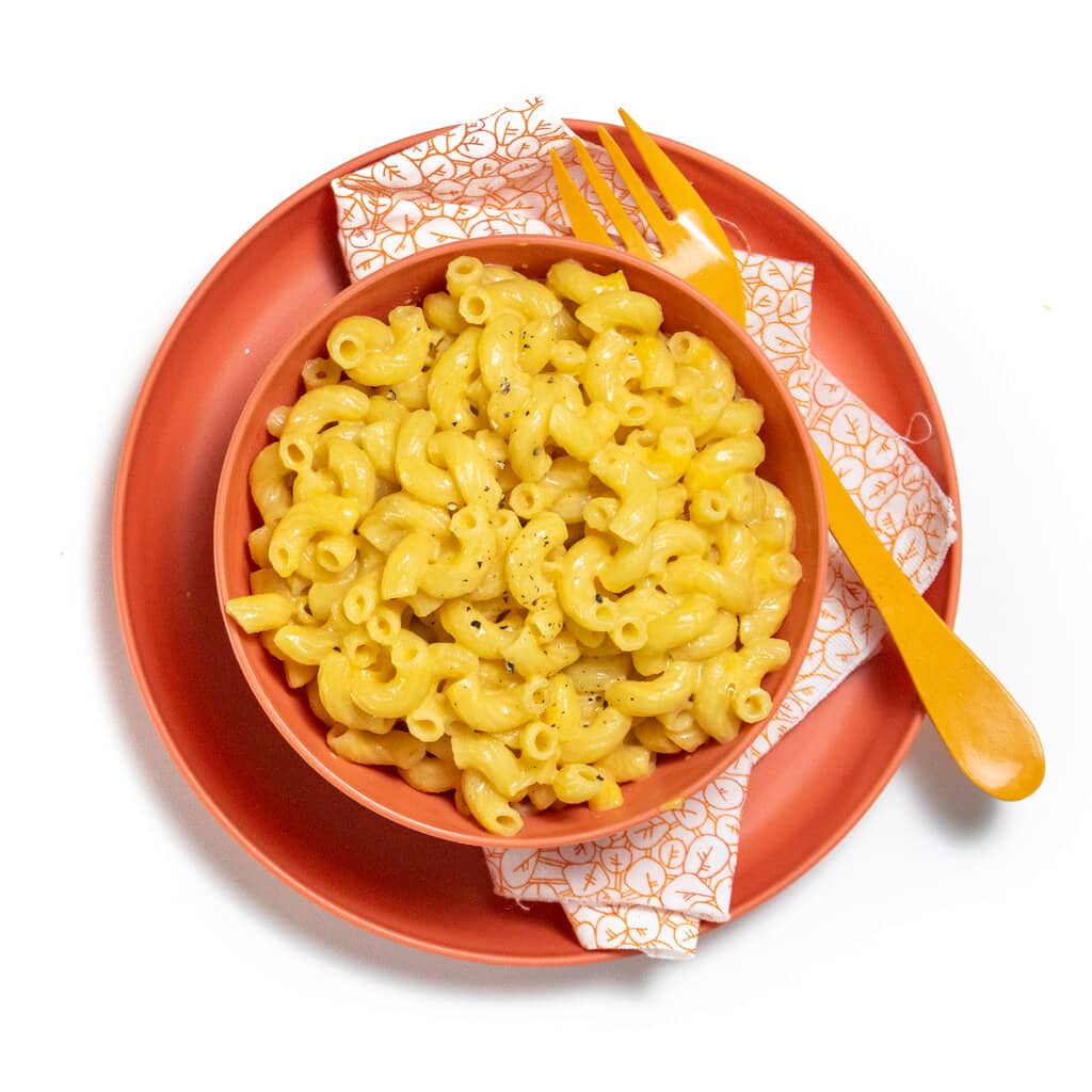 A pink kids, bowl and plate on a white countertop full of veggie mac & cheese.