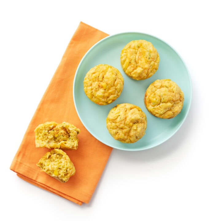 A blue kids plate with a colorful orange napkin with veggie muffins one torn in half to show the fluffy insides.