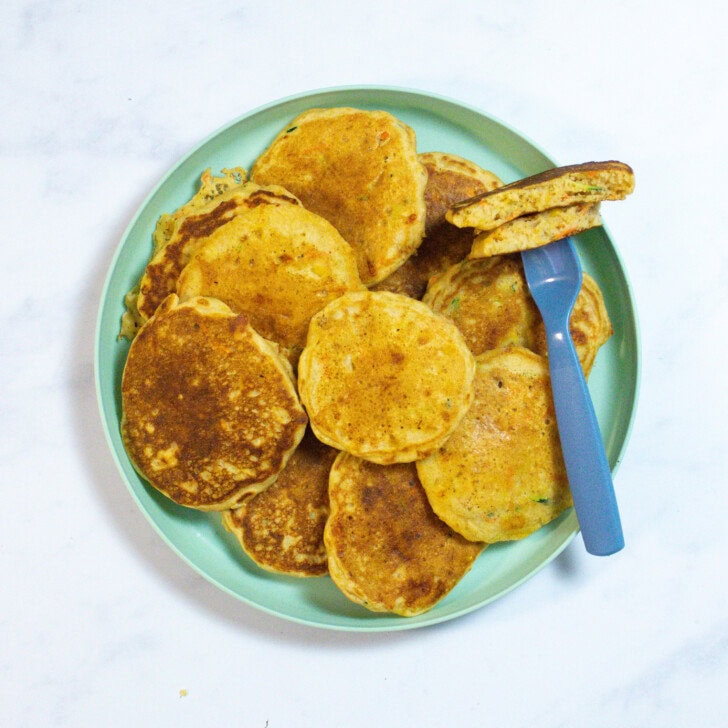 A plate full of veggie pancakes with a fork holding one cut and half on my kitchen counter.