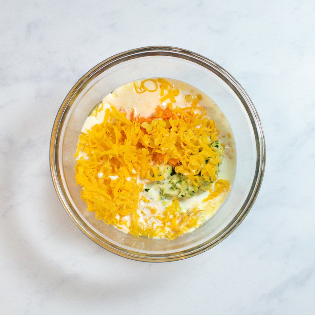 Clear glass mixing bowl on a white marble countertop in my kitchen with ingredients for veggie pancakes.