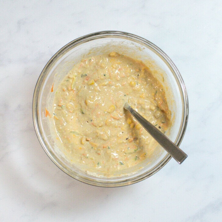 A clear mixing bowl on my kitchen counter with the ingredients for veggie pancakes, mixed and ready to be baked.