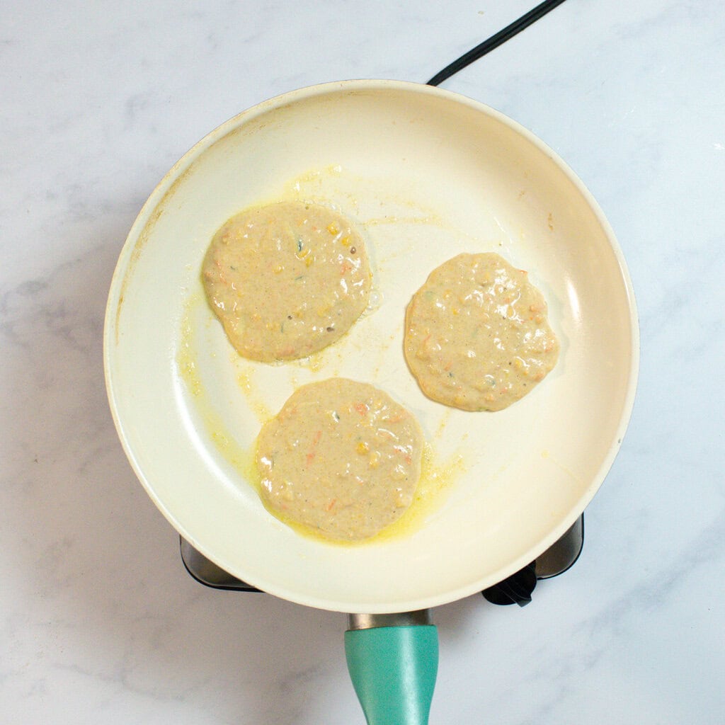 A white skillet with three veggie pancakes.