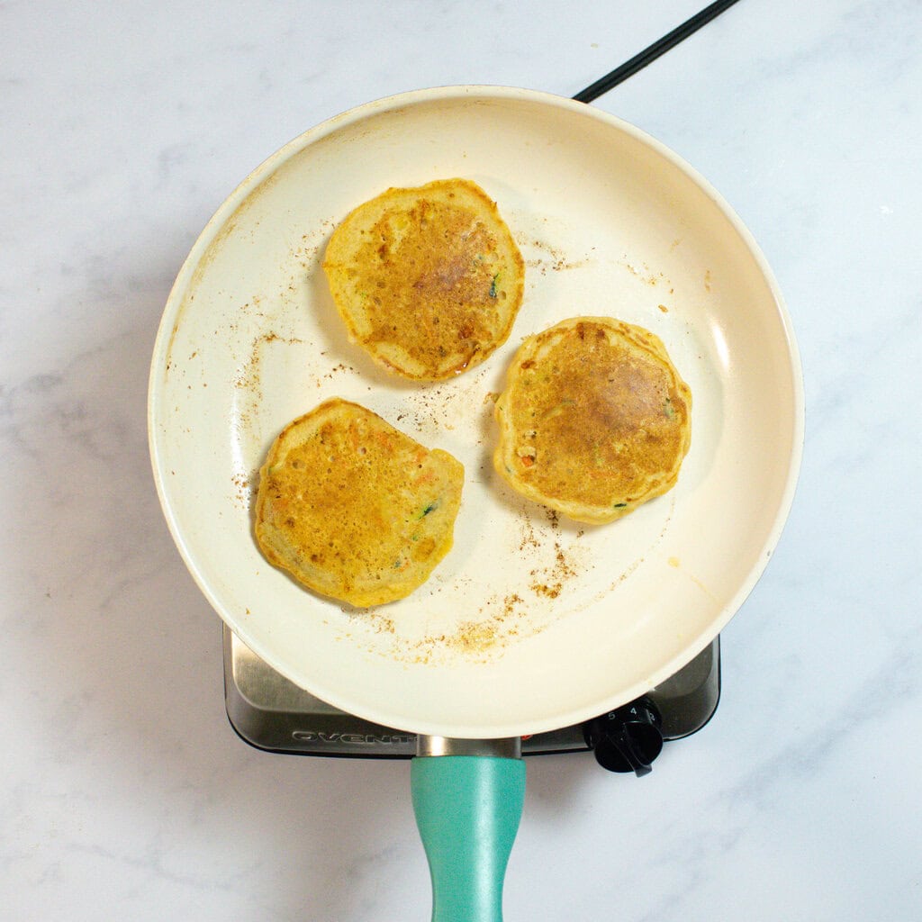 White skillet with three golden baked veggie pancakes.