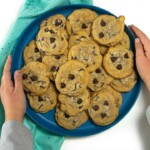 2 small kids hands holding a plate of whole wheat chocolate chip cookies.