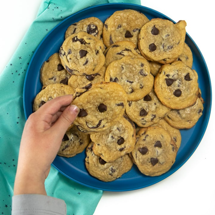 Small kids hands holding a whole wheat chocolate chip cookie over a plate of cookies. 