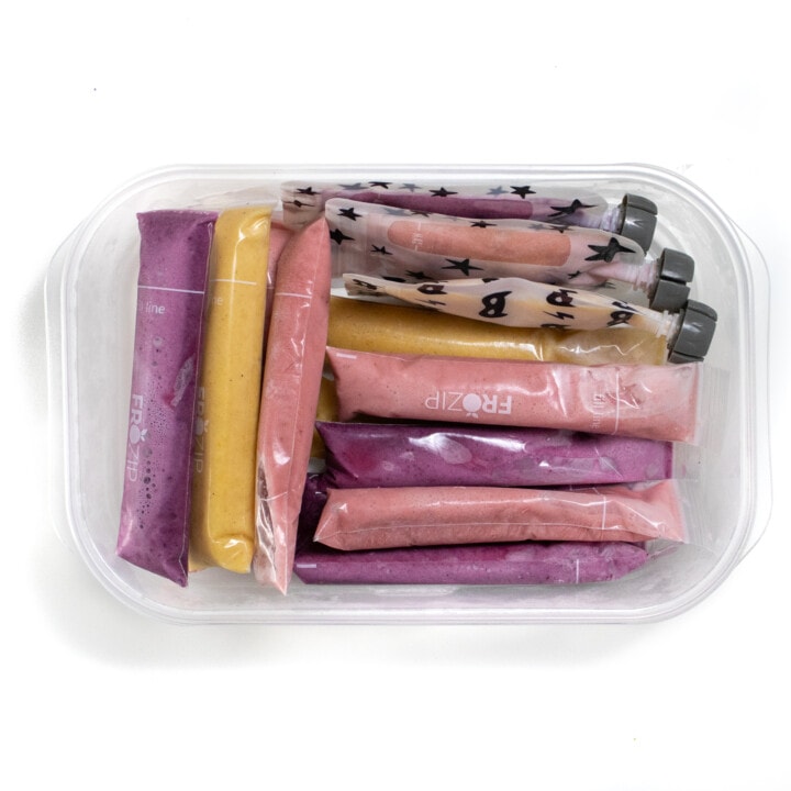 A white kitchen container filled with different yogurt tubes and pouches frozen.