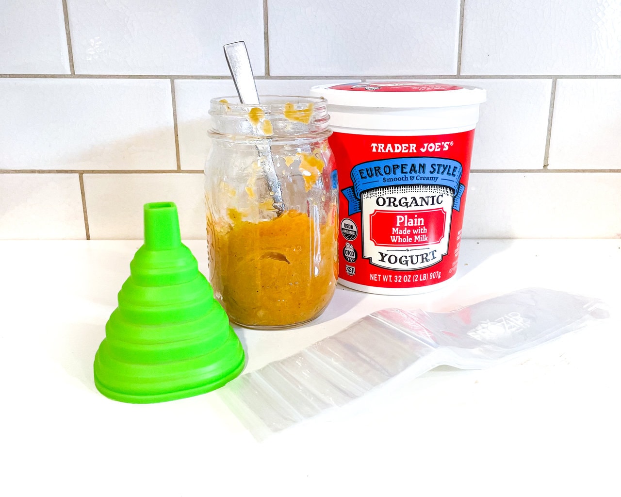 A white counter with a white tail background with yogurt peach preserves, yogurt tubes in a funnel.