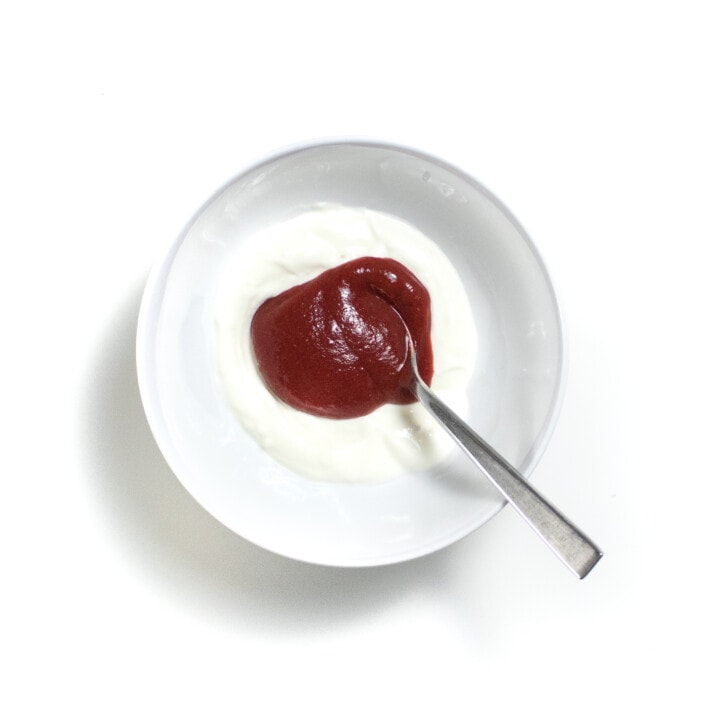 White bowl against a white background with yogurt and baby food purée inside.