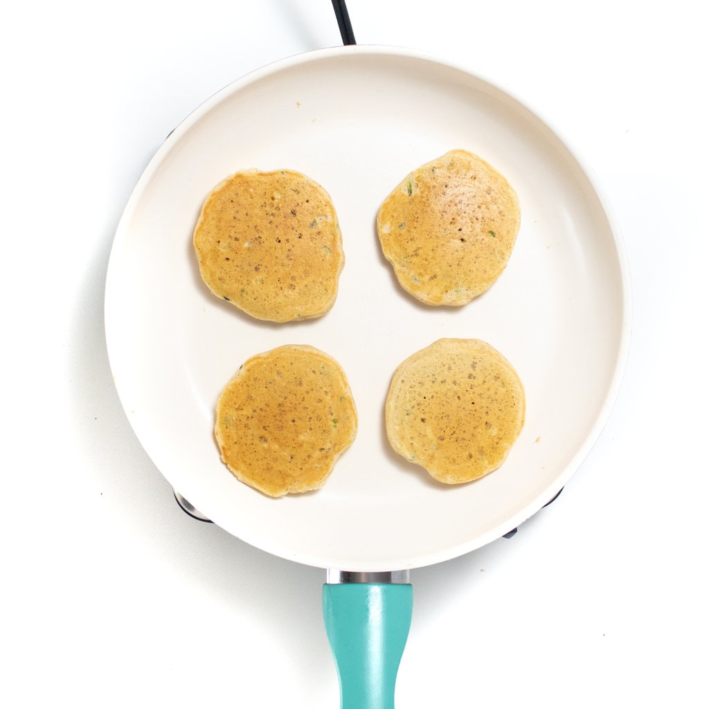 A skillet with four cooked zucchini pancakes.