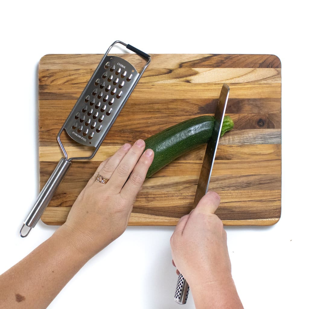 Two hands cutting the top of the zucchini off.