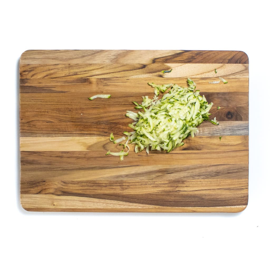 A wooden cutting board white background with a pile of grated zucchini.