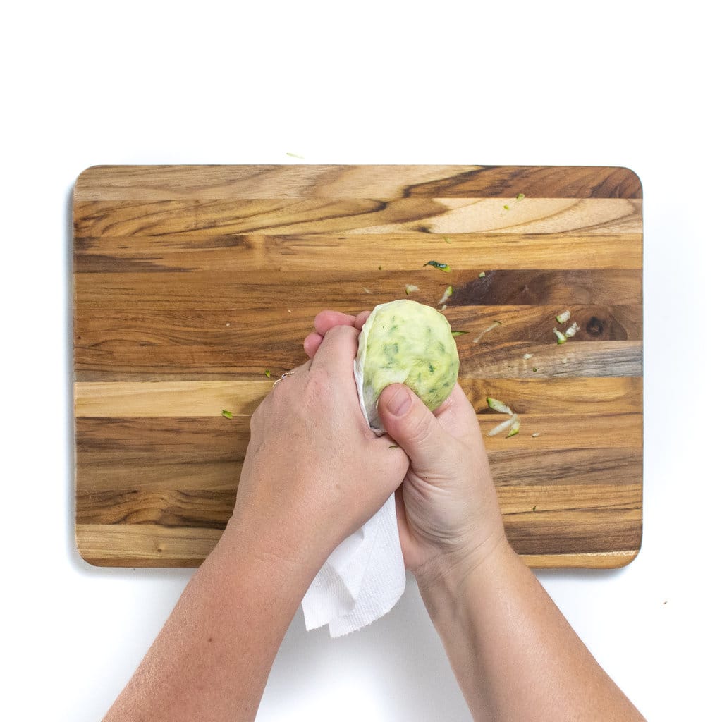 Hands holding a paper towel with grated zucchini getting the water out of it.