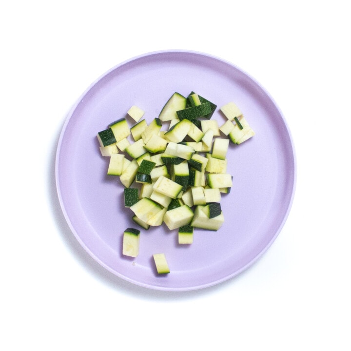 A bright purple kids plate with chopped zucchini.