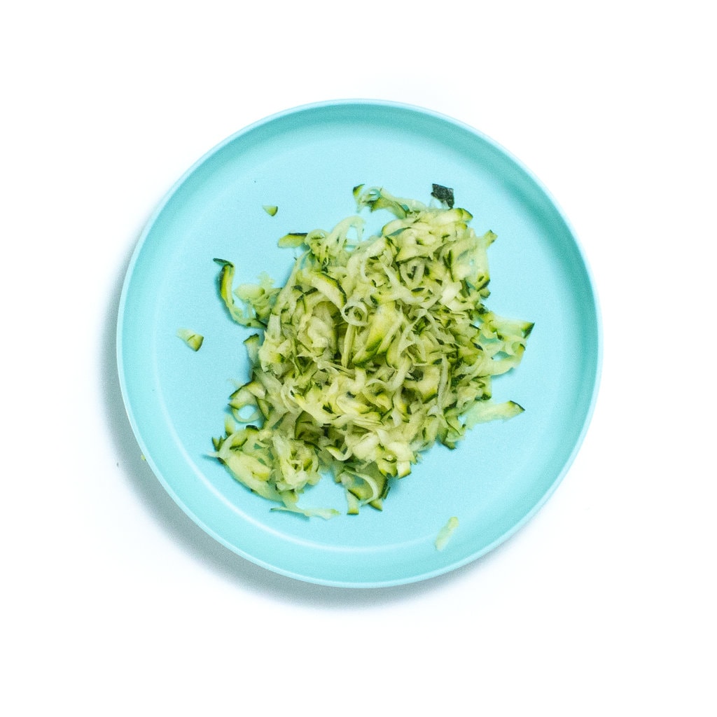 A bright blue kids play with grated zucchini.