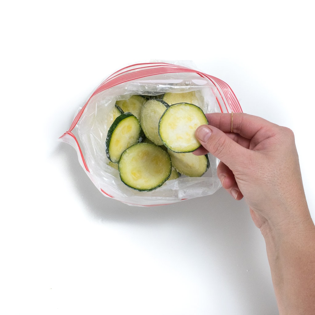 A hand holding up a frozen slice of zucchini.